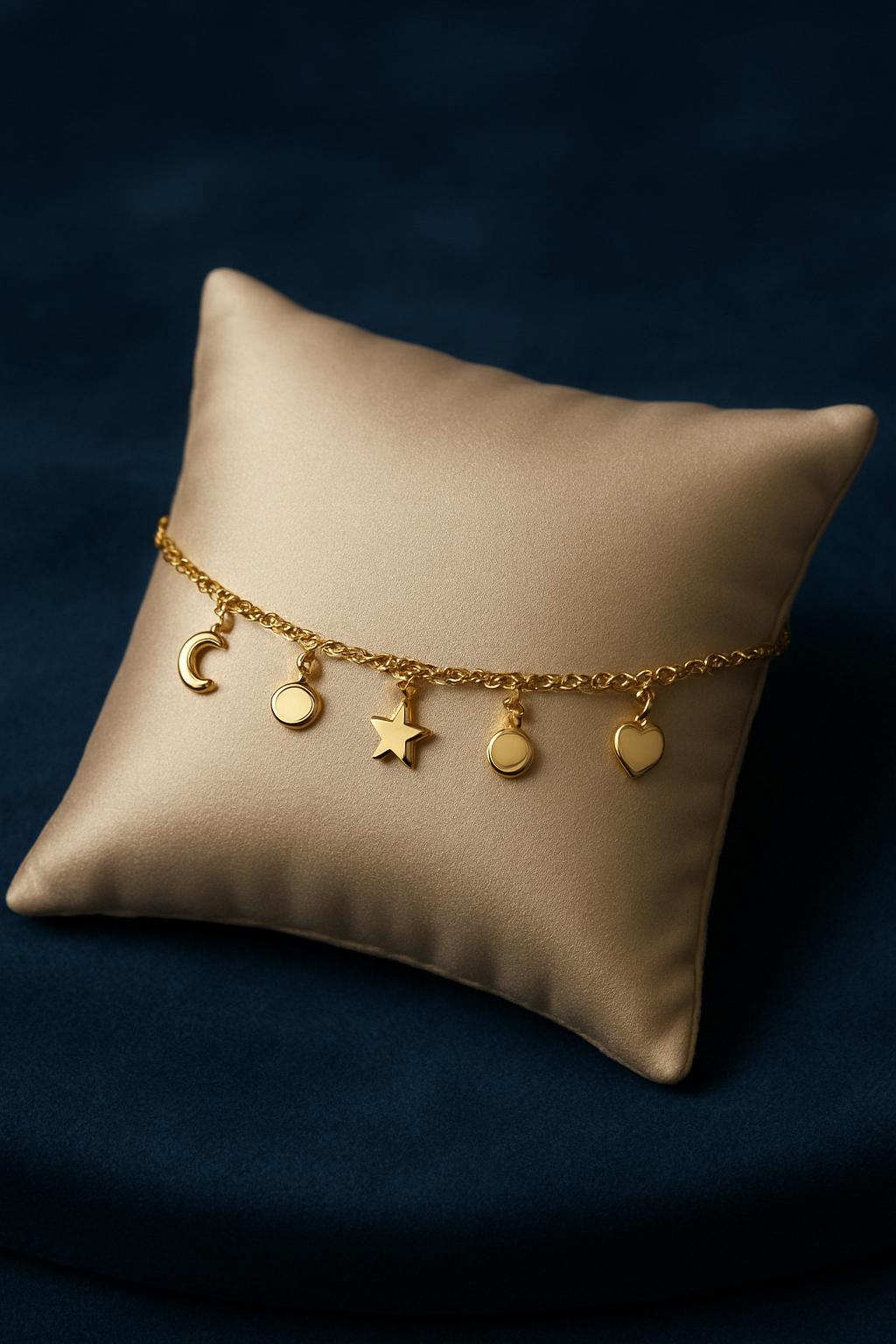 The image features a gold bracelet with five pendants resting on a beige silk or satin pillow. The pendants, from left to ...